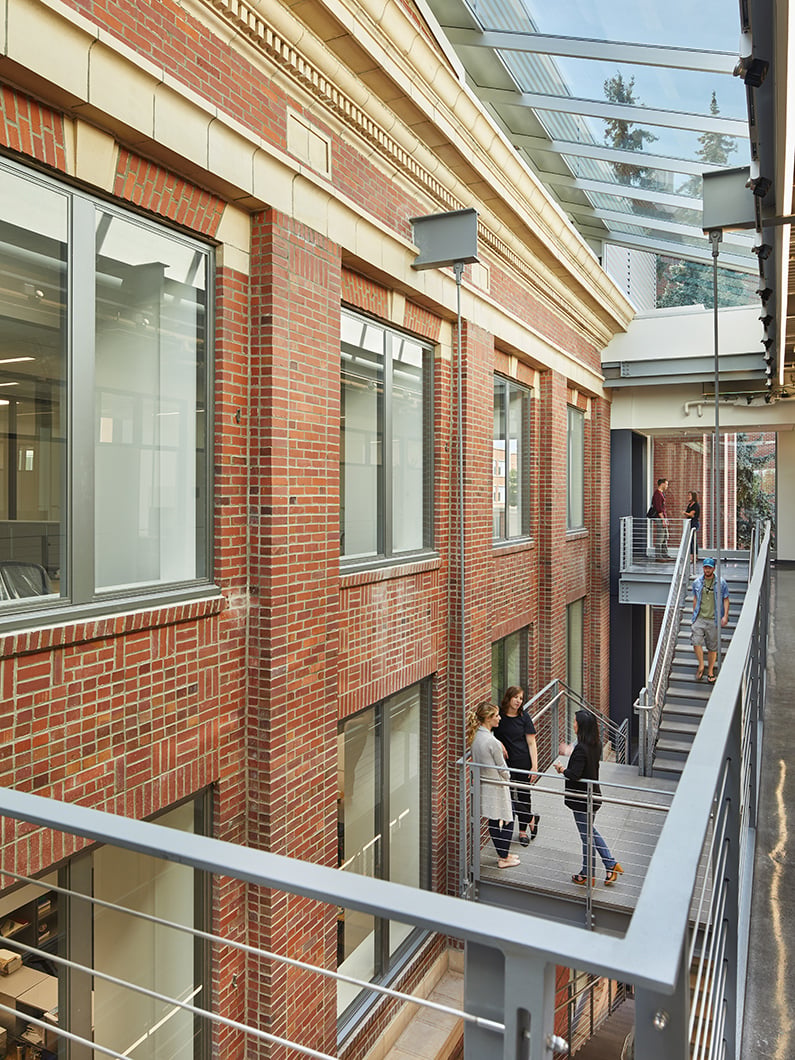 3 students gathered at the top of the stairs in the atrium with skylight above.