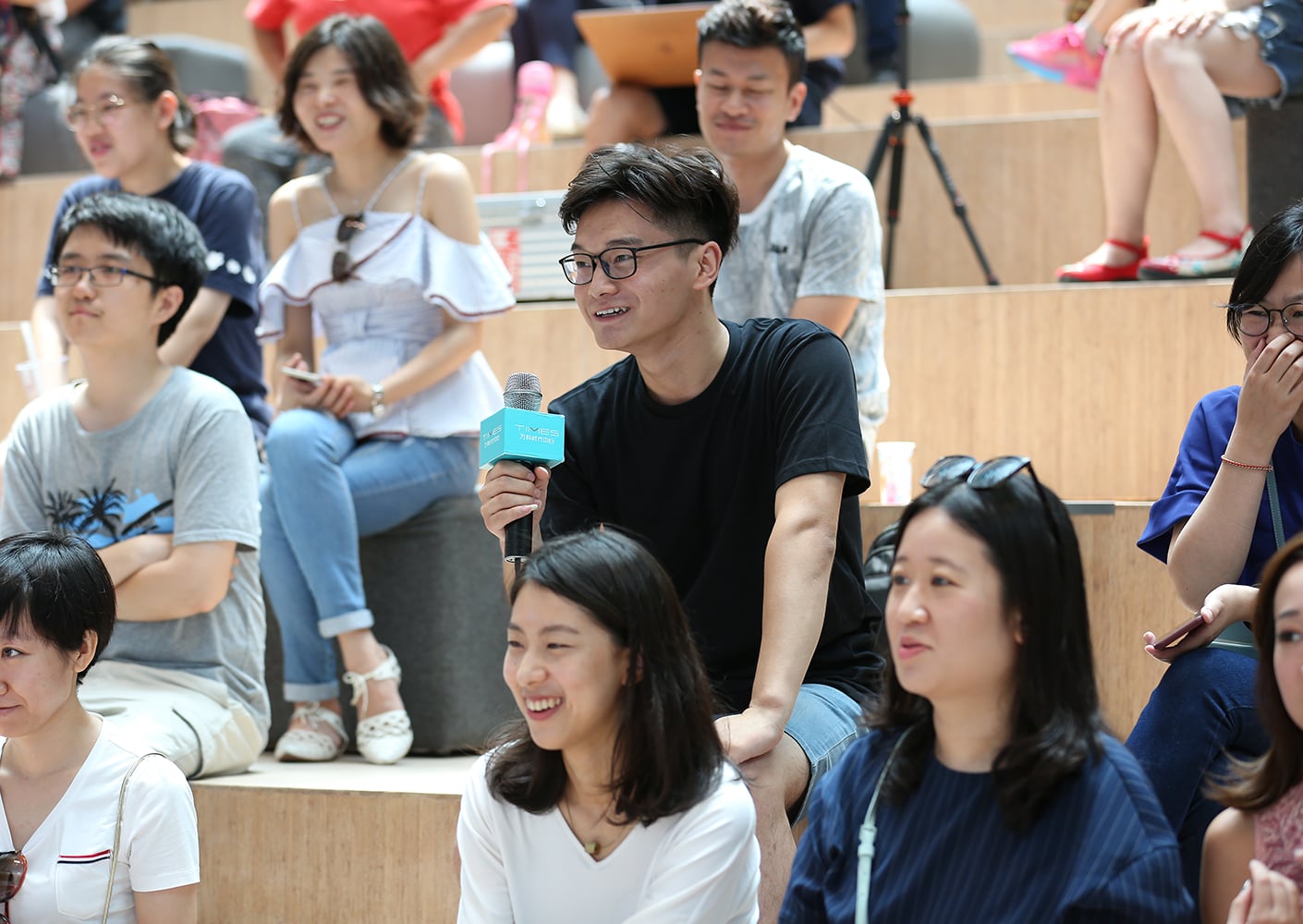Audience seated on tiered wooden steps in an open space, enhancing acoustics and visibility for discussions in a vibrant, communal environment.
