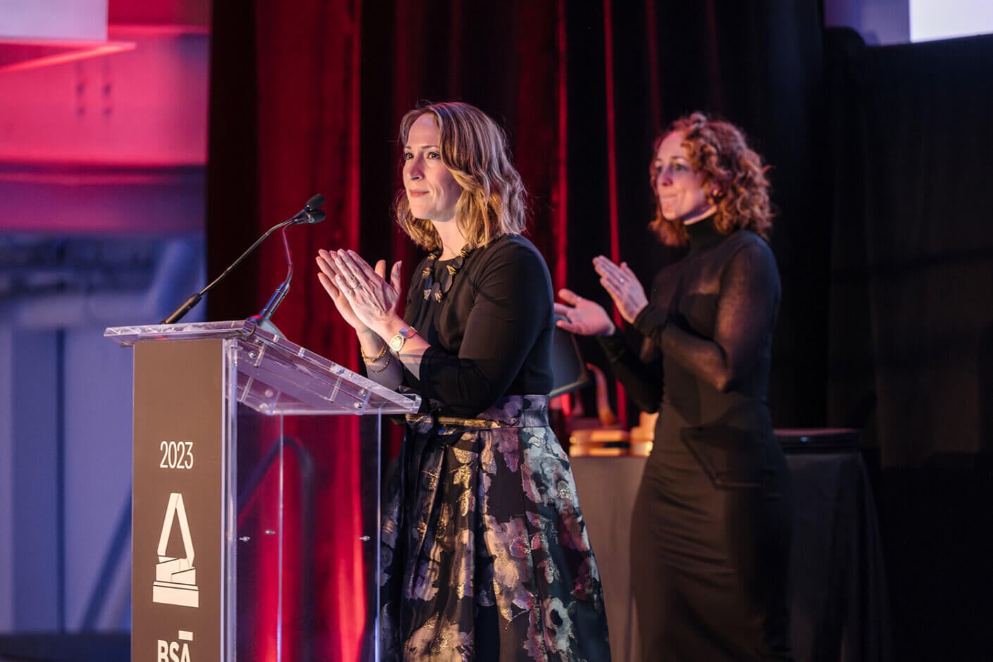 Yanel speaking at an awards ceremony, with a supportive colleague beside her.