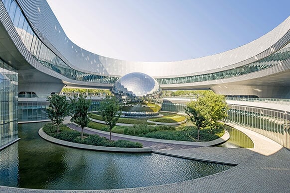 Architectural design featuring a reflective sphere surrounded by greenery and water within a structured landscape. Clear sky overhead.