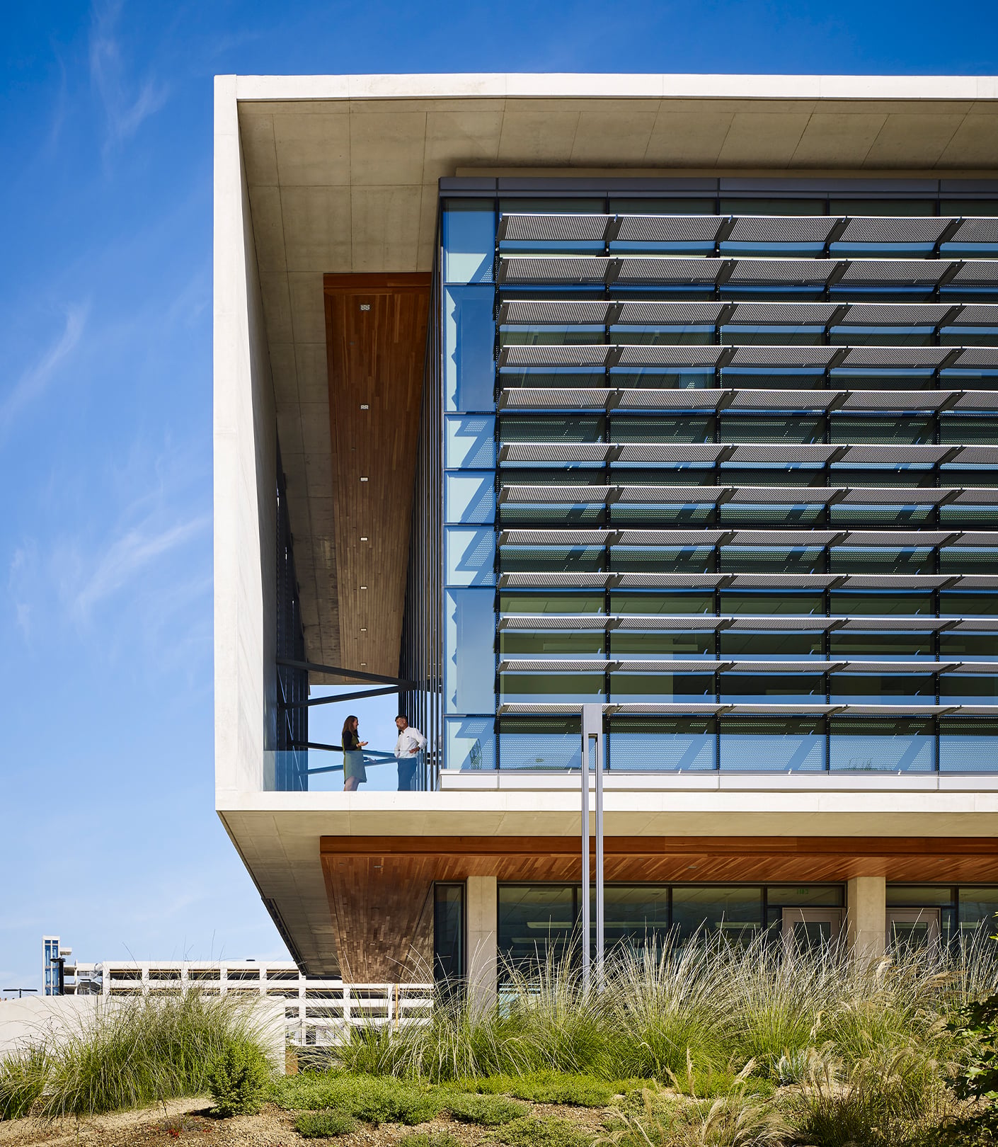 Exterior view of south west corner with two people standing and talking on outdoor balcony.