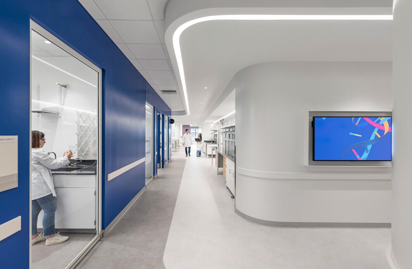 Lab corridor with people walking down and person working in lab space