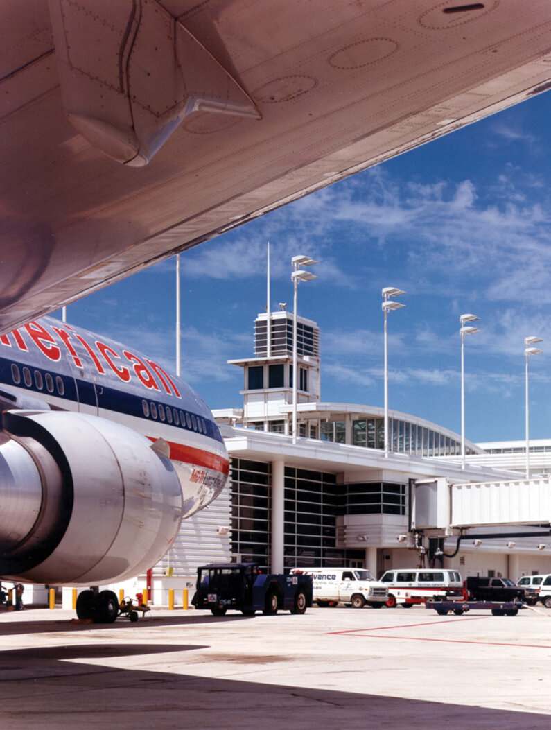 Photograph view of air control tower rising from Terminal D building from under the wing of an airplane