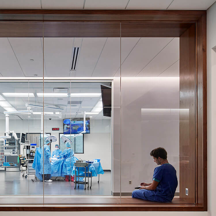Photo showing medical student in the foreground and a large window with a view into a mock operating room