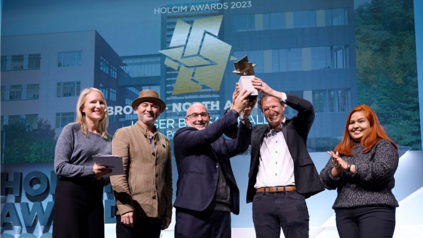 Five people on a stage. Two are holding an award above their heads.