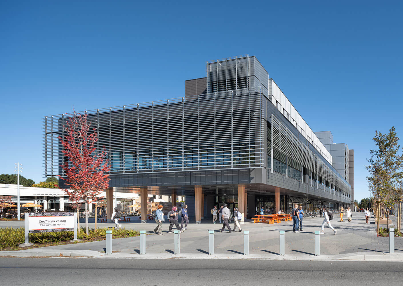 A photograph of Cheko’nien House from Ring Road looking down the Campus Greenway with students walking in the foreground.