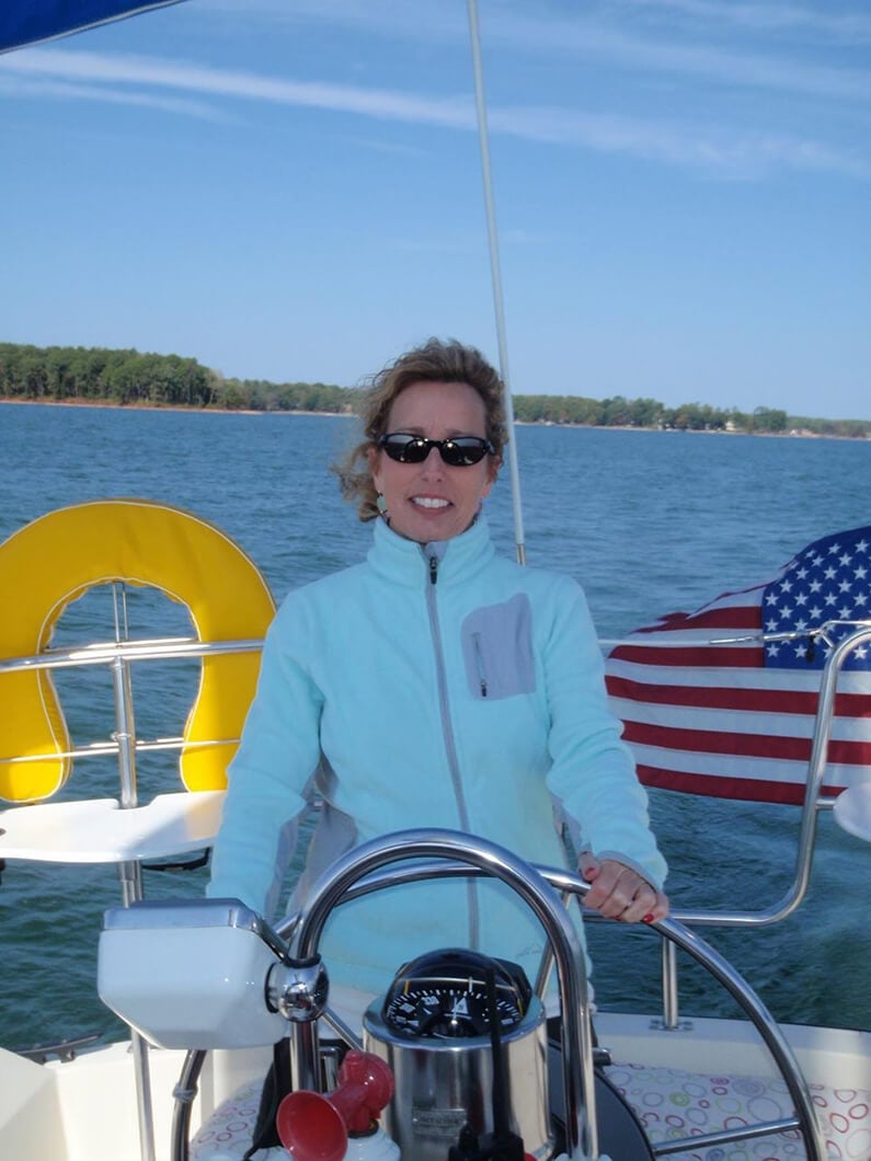 Debbie smiling at the helm of a sailboat