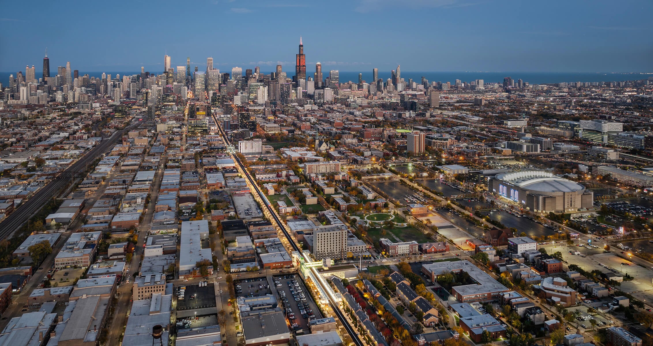 Aerial view of Chicago skyline at dusk with illuminated streets and Lake Michigan in the background.