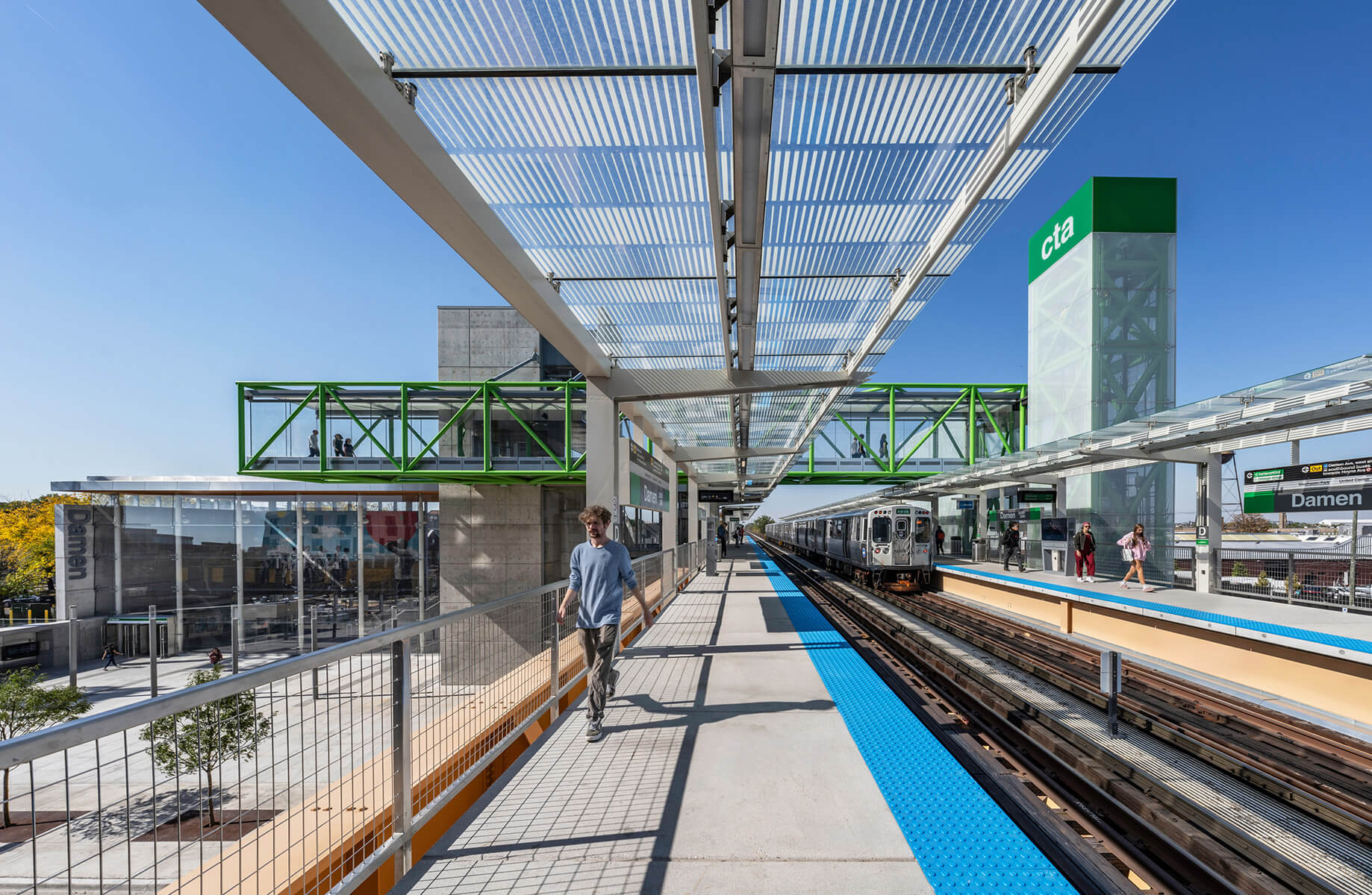 Modern train station platform with people, green structure, and train arriving.