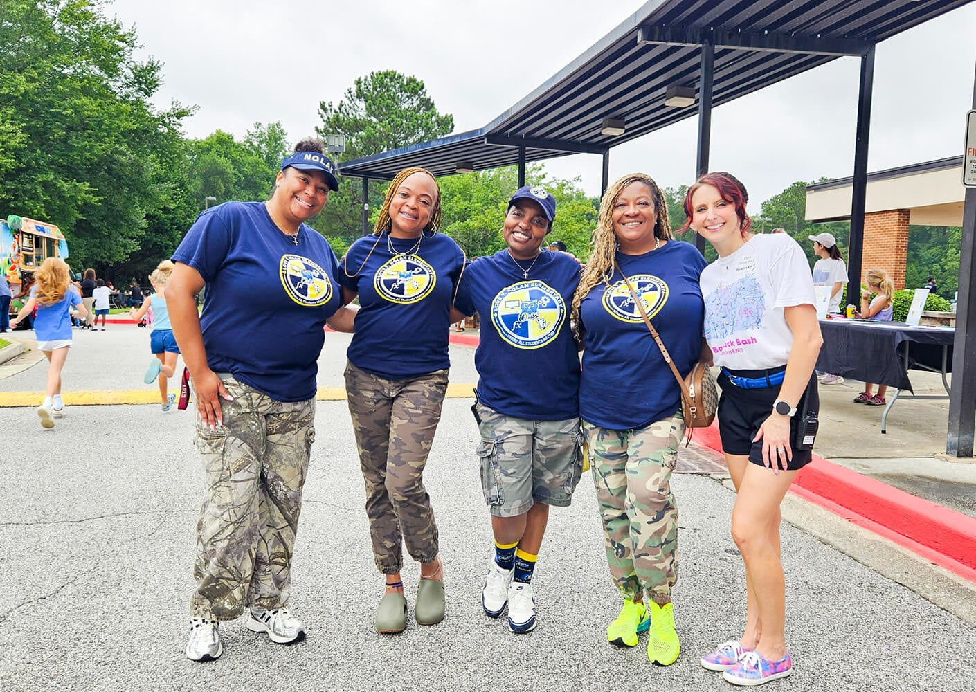 Five women smiling in front of an elementary school