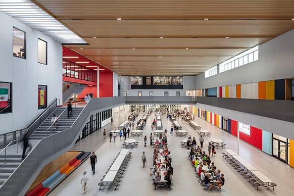 Modern school cafeteria and atrium with students, vibrant colors, and natural light from multiple directions.