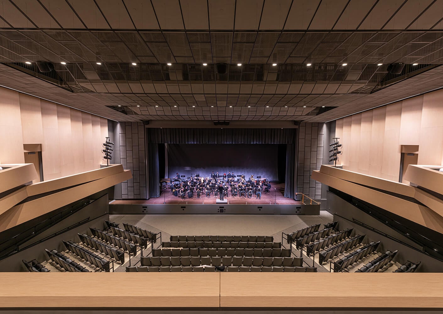 Wide view of a concert hall with an orchestra on stage, showcasing modern architecture and ample seating.