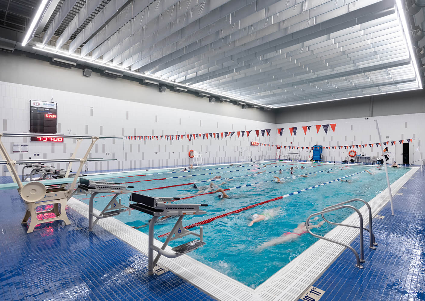 Indoor school swimming pool with lane dividers and swimmers practicing under bright lighting.