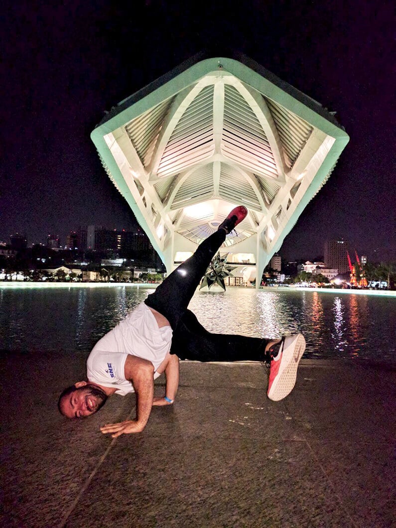 Man doing a breakdance freeze in front of an illuminated modern building at night.