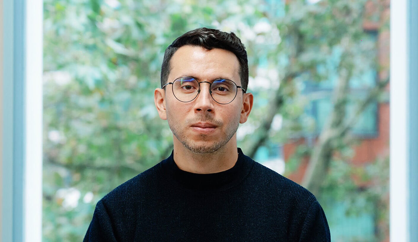 Person with glasses in front of a window with trees in the background.