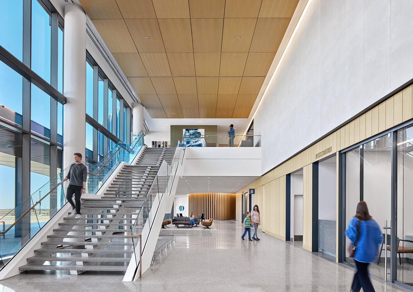 Modern hospital lobby with staircase, large windows, and people walking.