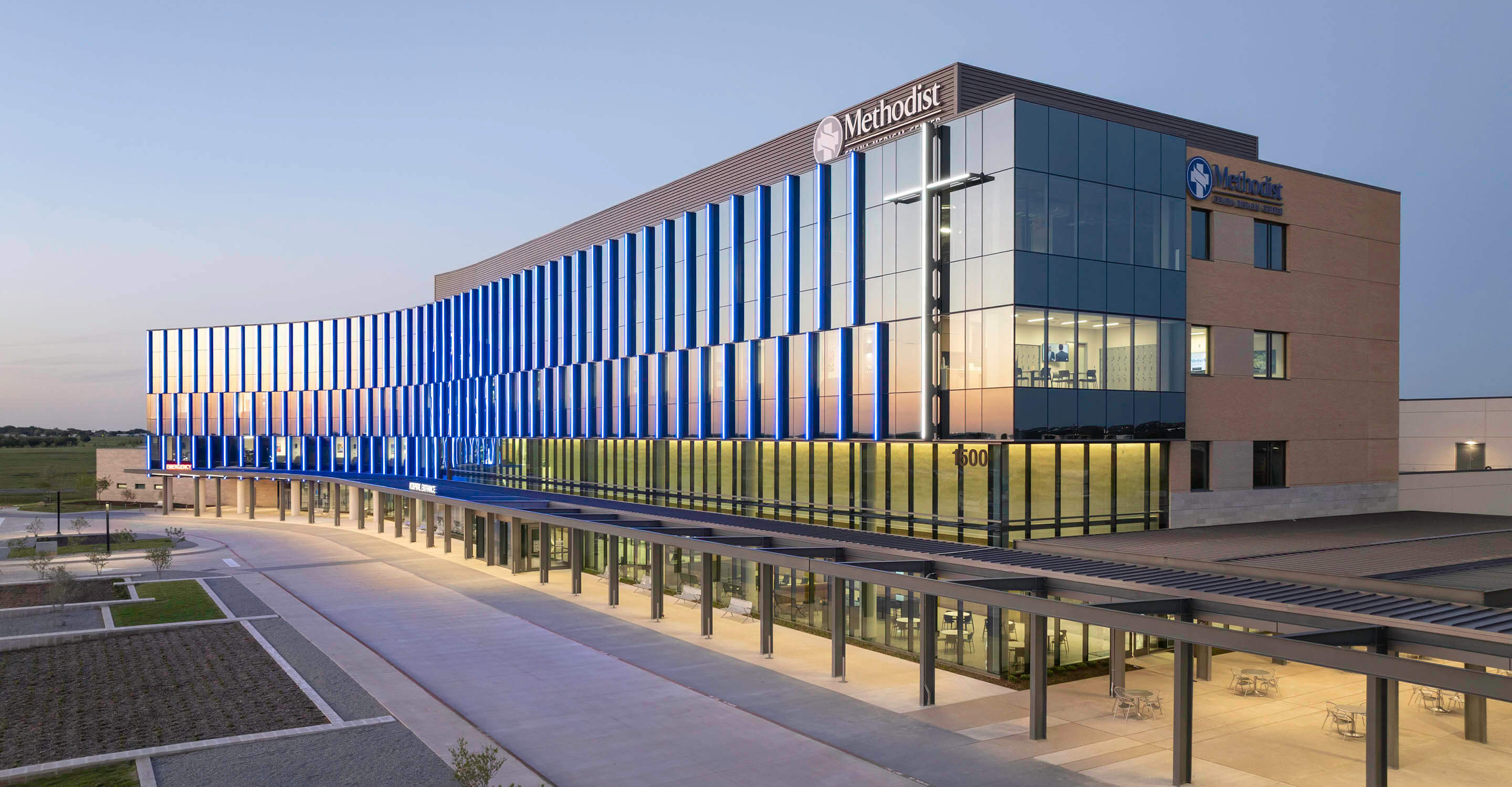 Modern hospital building exterior at dusk with blue-lit windows.