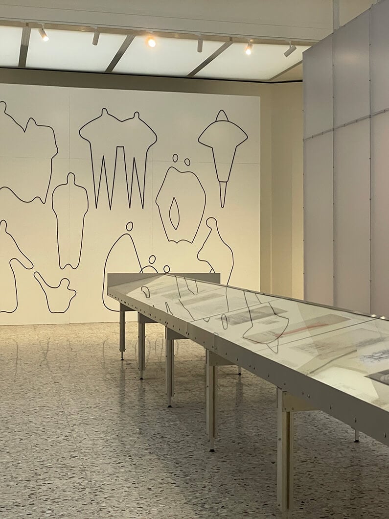 Minimalist gallery exhibit with abstract line art on walls and glass display cases.