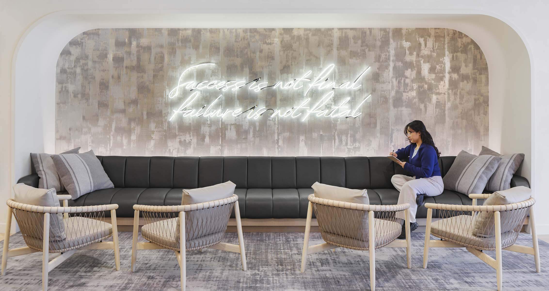 Modern lounge with motivational quote and woman writing on a sofa.