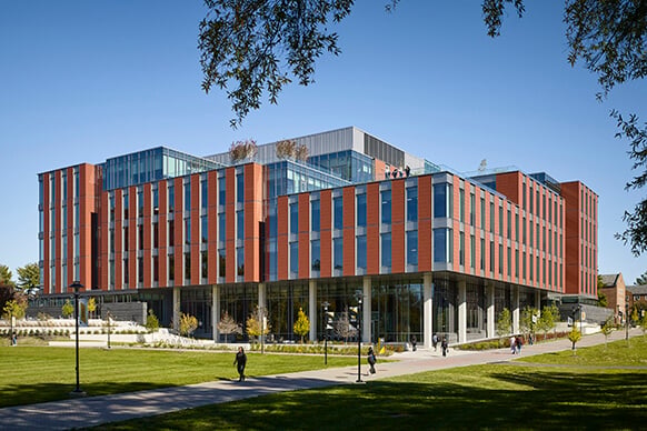 Modern university building with red brick facade and large glass windows on a sunny day.