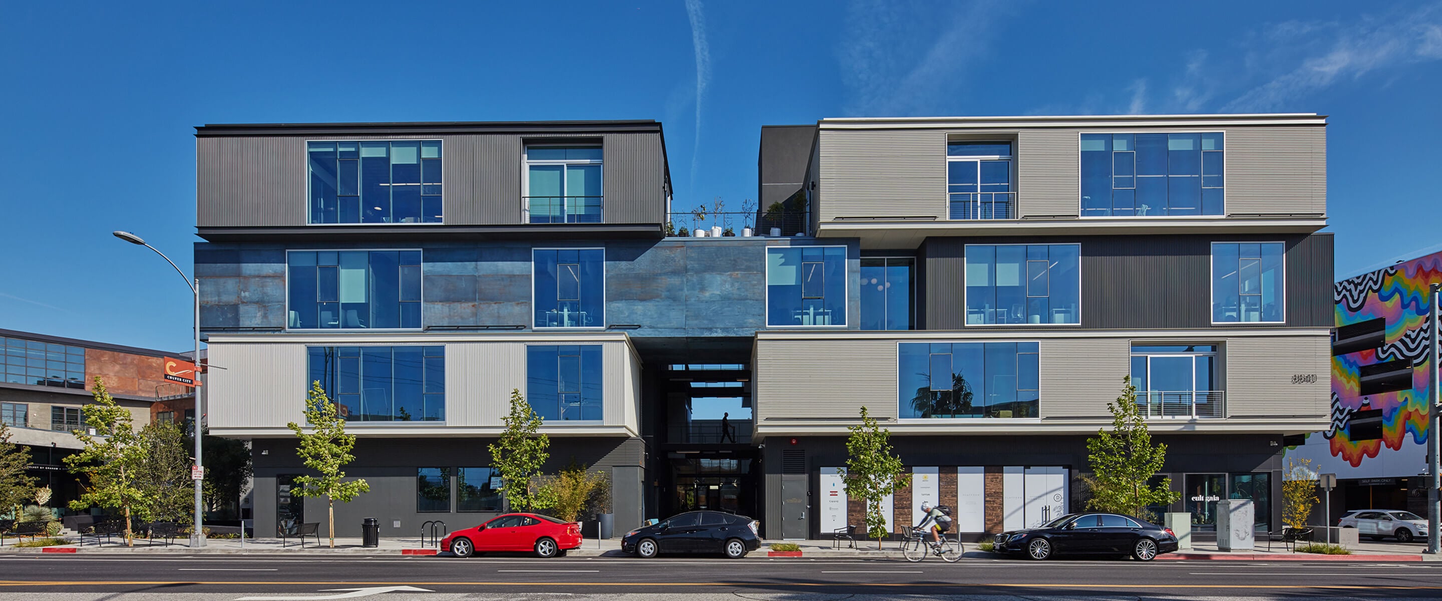 Modern building exterior with glass windows, parked cars, and vibrant street art.