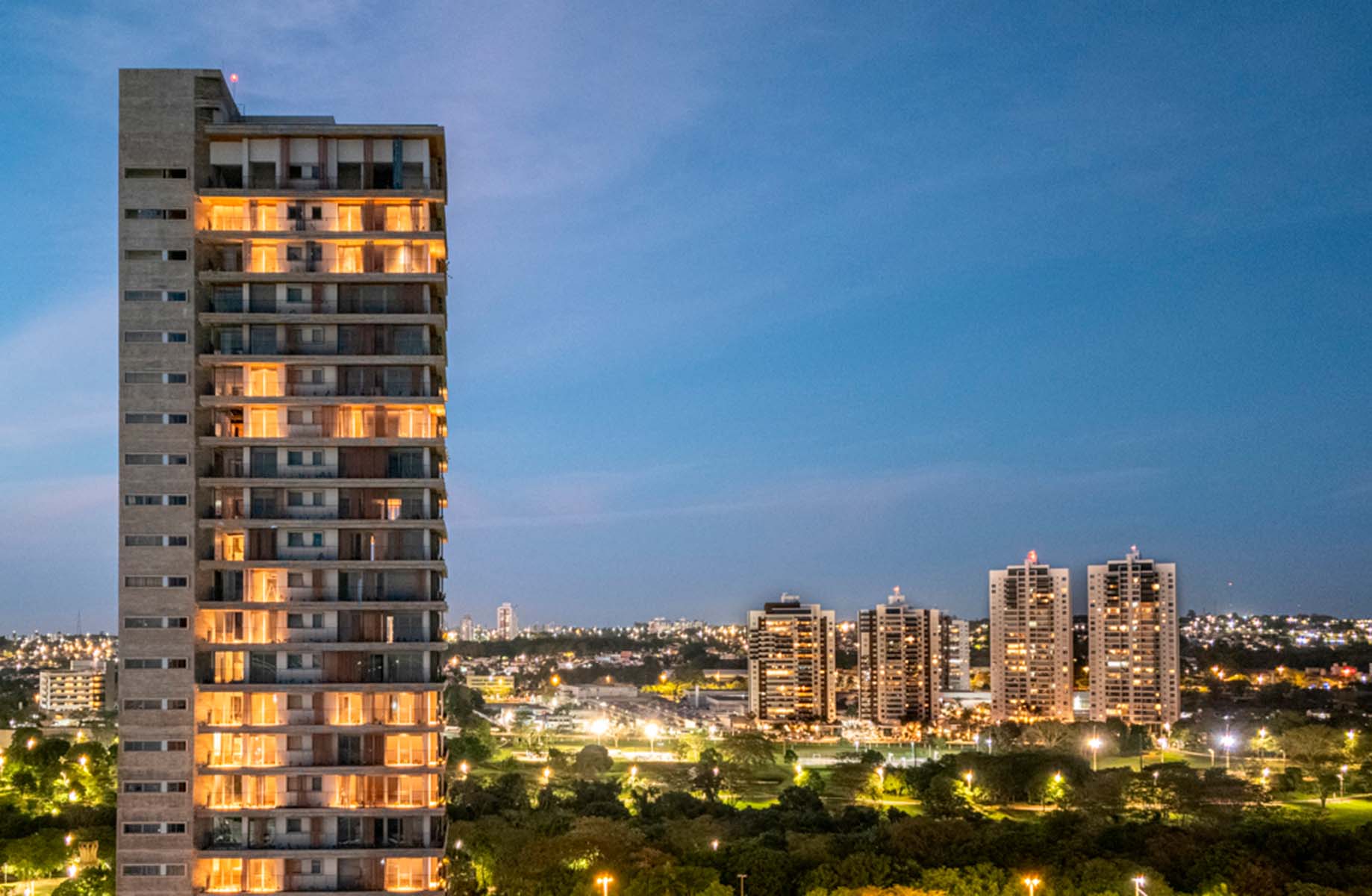 Tall illuminated buildings against a city skyline at dusk.