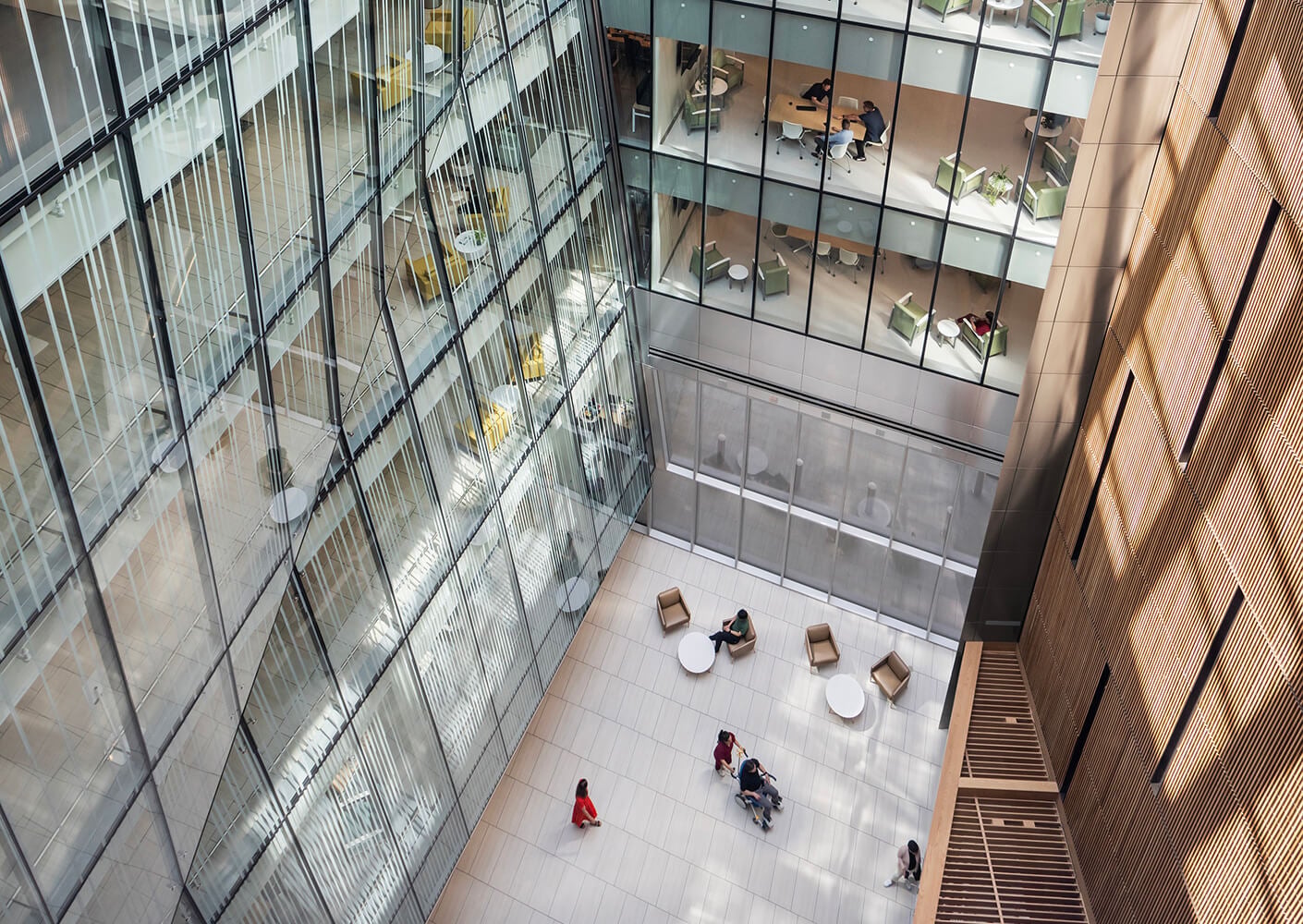 Modern office atrium with glass walls, people gathered around circular tables.