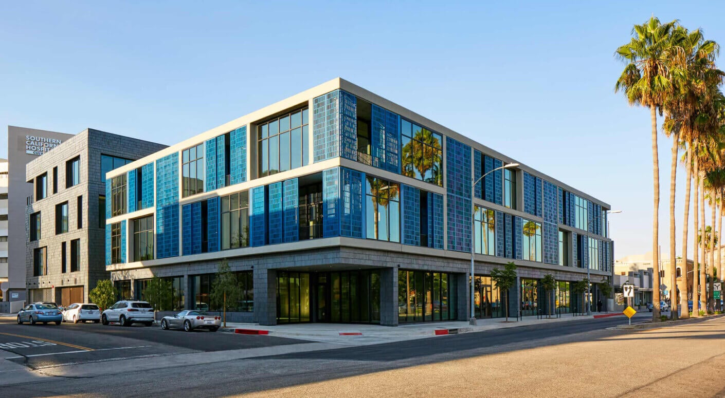 Modern urban building with blue glass facade, palm trees in sunlight.