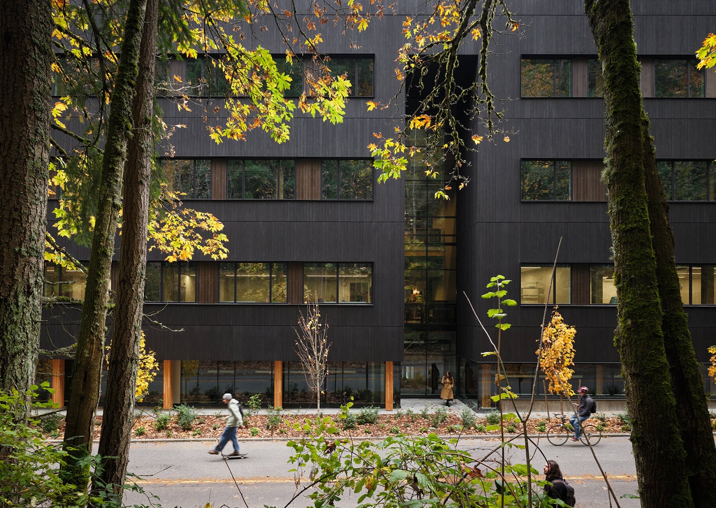 Modern building with fall foliage, people walking and cycling in an urban forest environment.