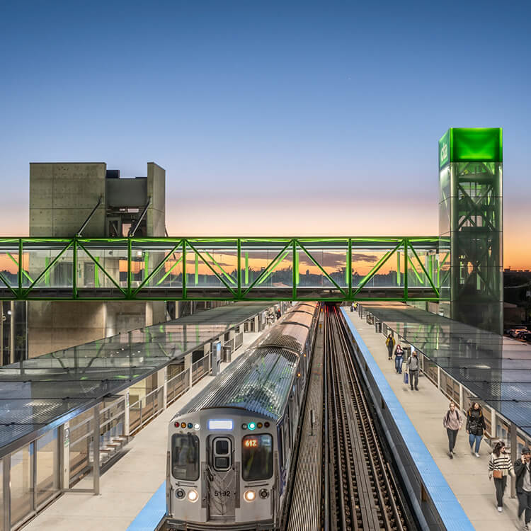 Modern train station at sunset with green walkway and passengers boarding.