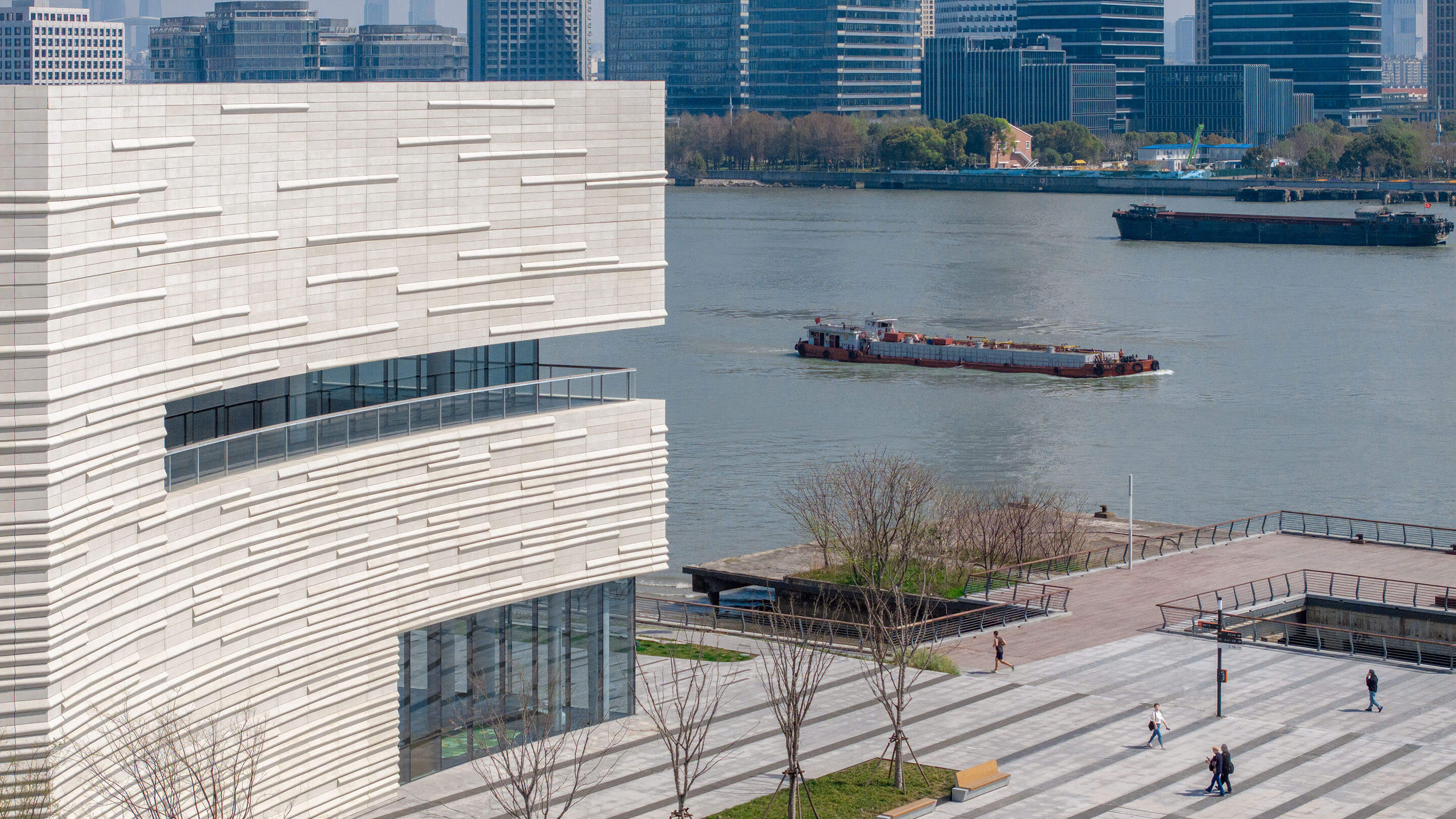 Modern riverside building with barge and skyline in the background.