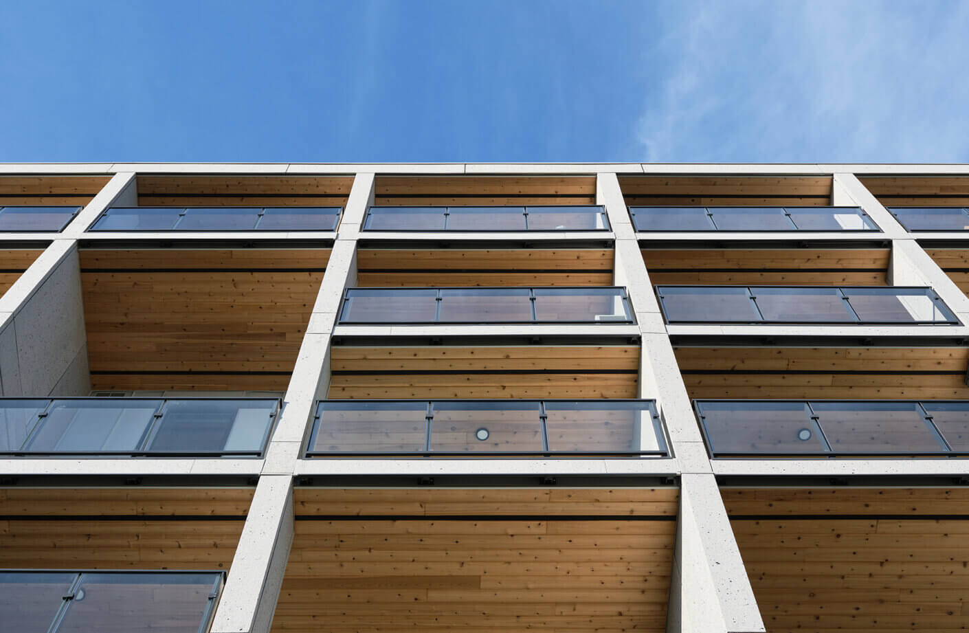 Modern apartment balconies with glass railings, blue sky background.