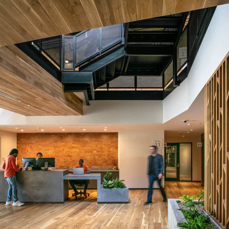 Modern office lobby with two receptionists, wooden accents, and a central staircase.