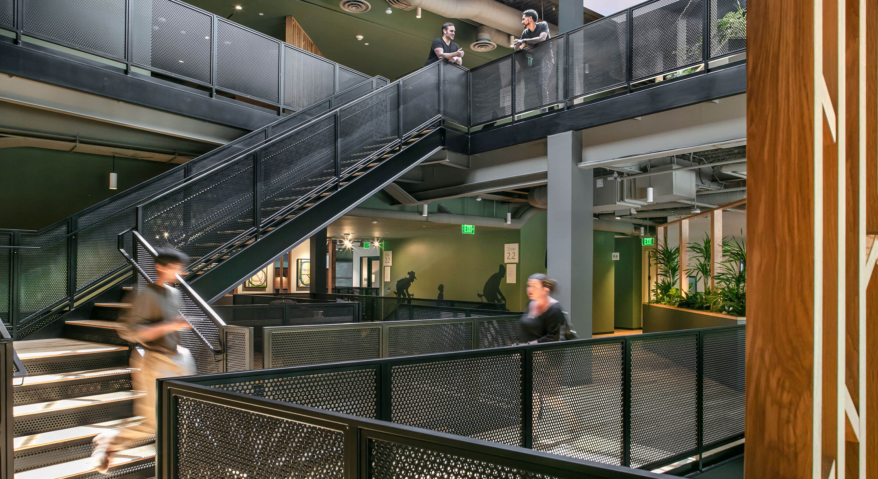 Modern office interior with people on stairs and walkway, green walls and plants.