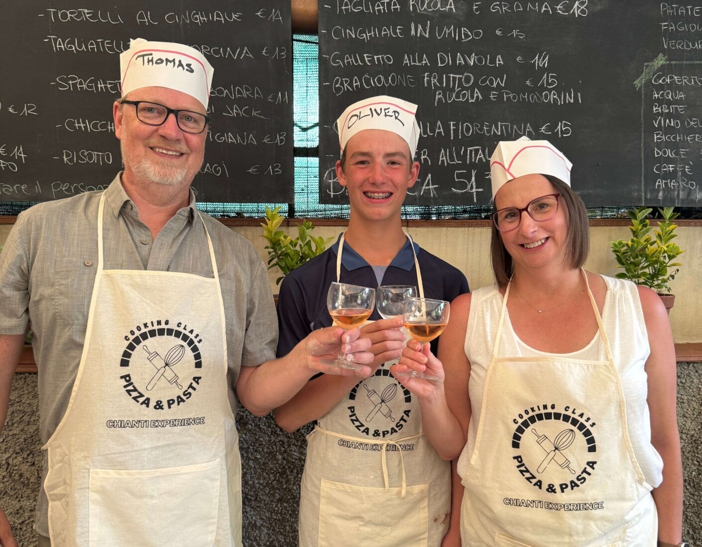 Tom with his wife and son in aprons celebrate with wine glasses in a cooking class setting.