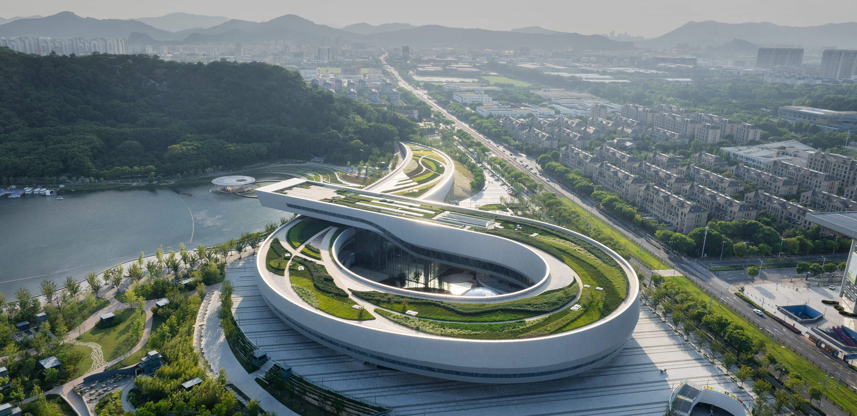 Aerial view of the ribbon-shaped Suzhou Museum of Science and Technology surrounded by green landscapes and cityscape.