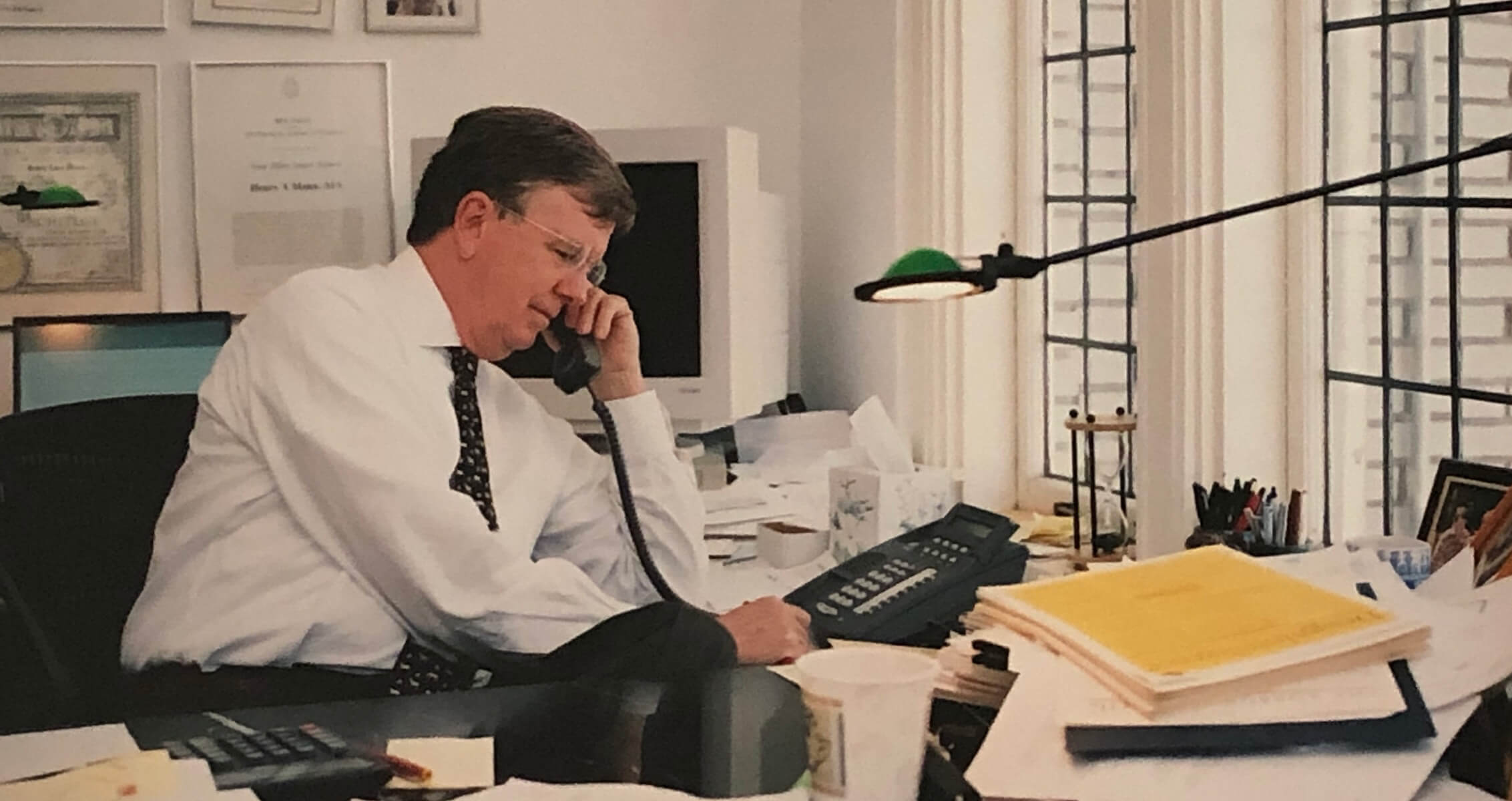 Henry Mann on the phone at a cluttered desk with papers and a computer.