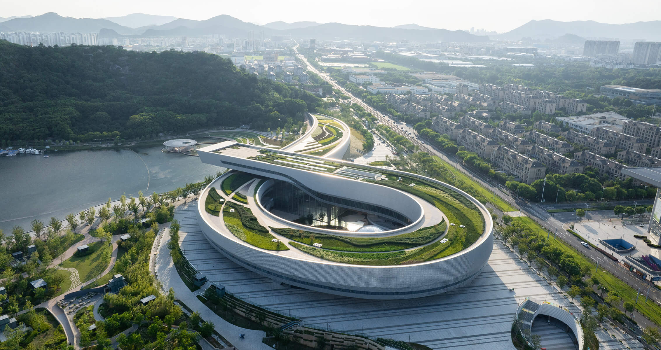 Aerial view of a modern museum surrounded by greenery and cityscape.