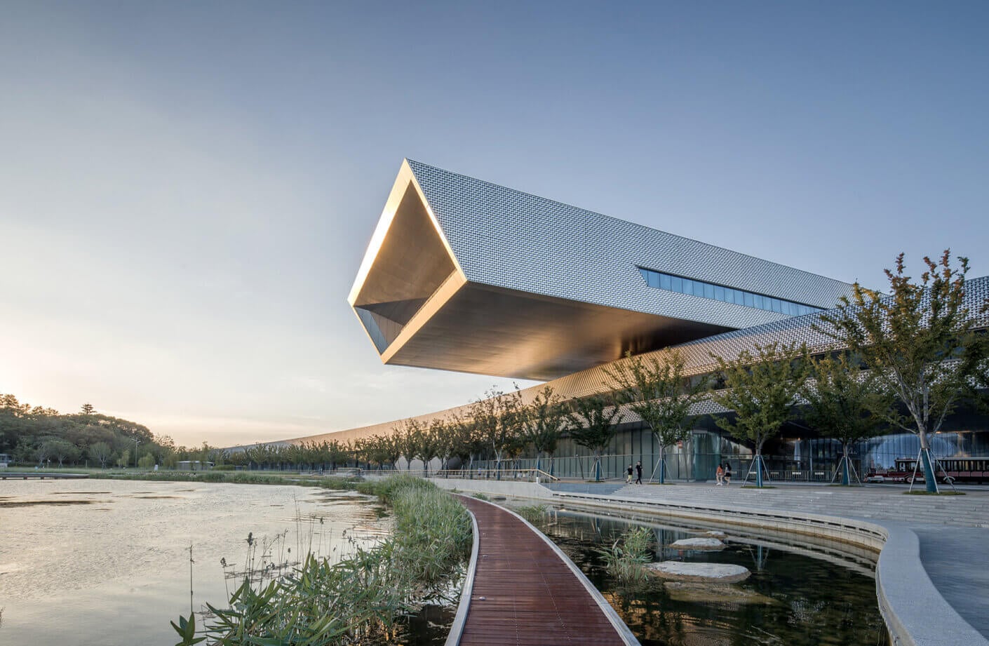 Modern museum cantilevers over a serene pond during sunset.