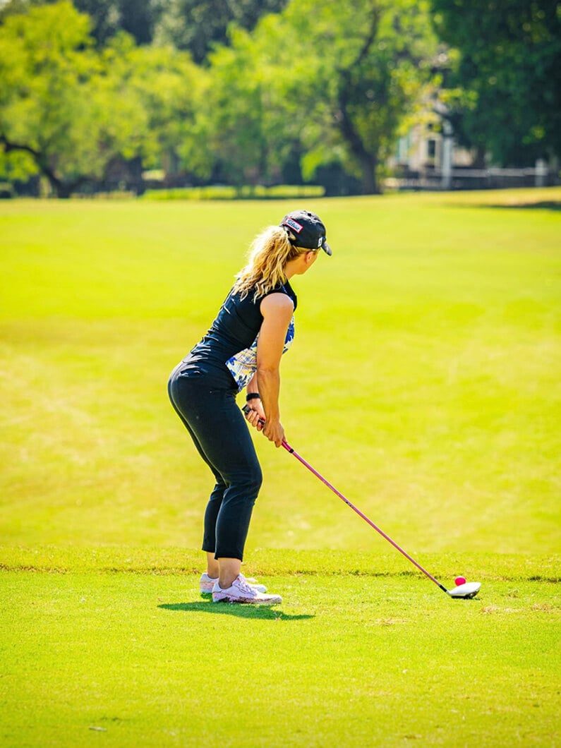 Andrea preparing to tee off on a golf course in sunny weather.