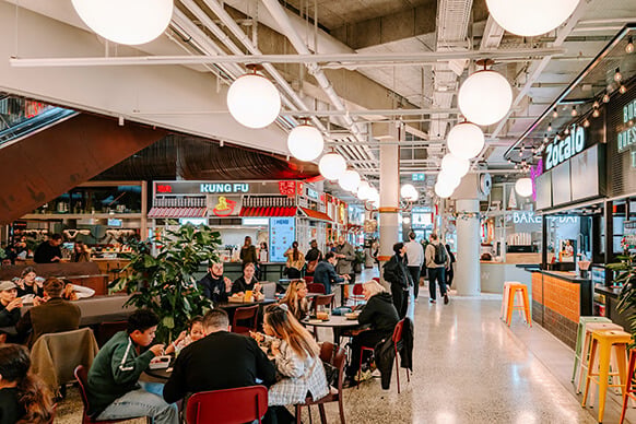 Vibrant food market bustling with diners and diverse food stalls under glowing lights.
