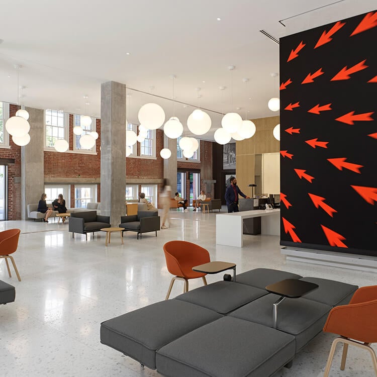 Interior view of a spacious lobby featuring large light fixtures, contemporary seating, and a bold arrow-patterned wall. Patrons are engaged in conversation.