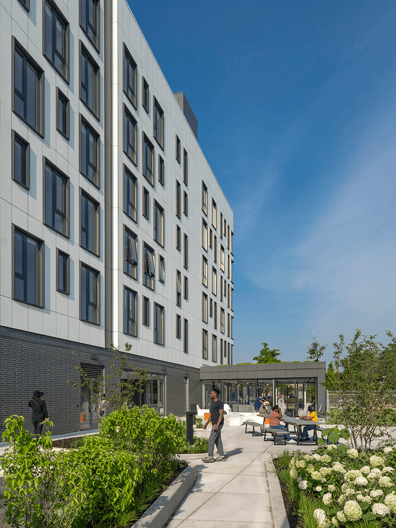 Exterior view of a multi-story building with large windows, showcasing landscaping and people interacting in an outdoor area.