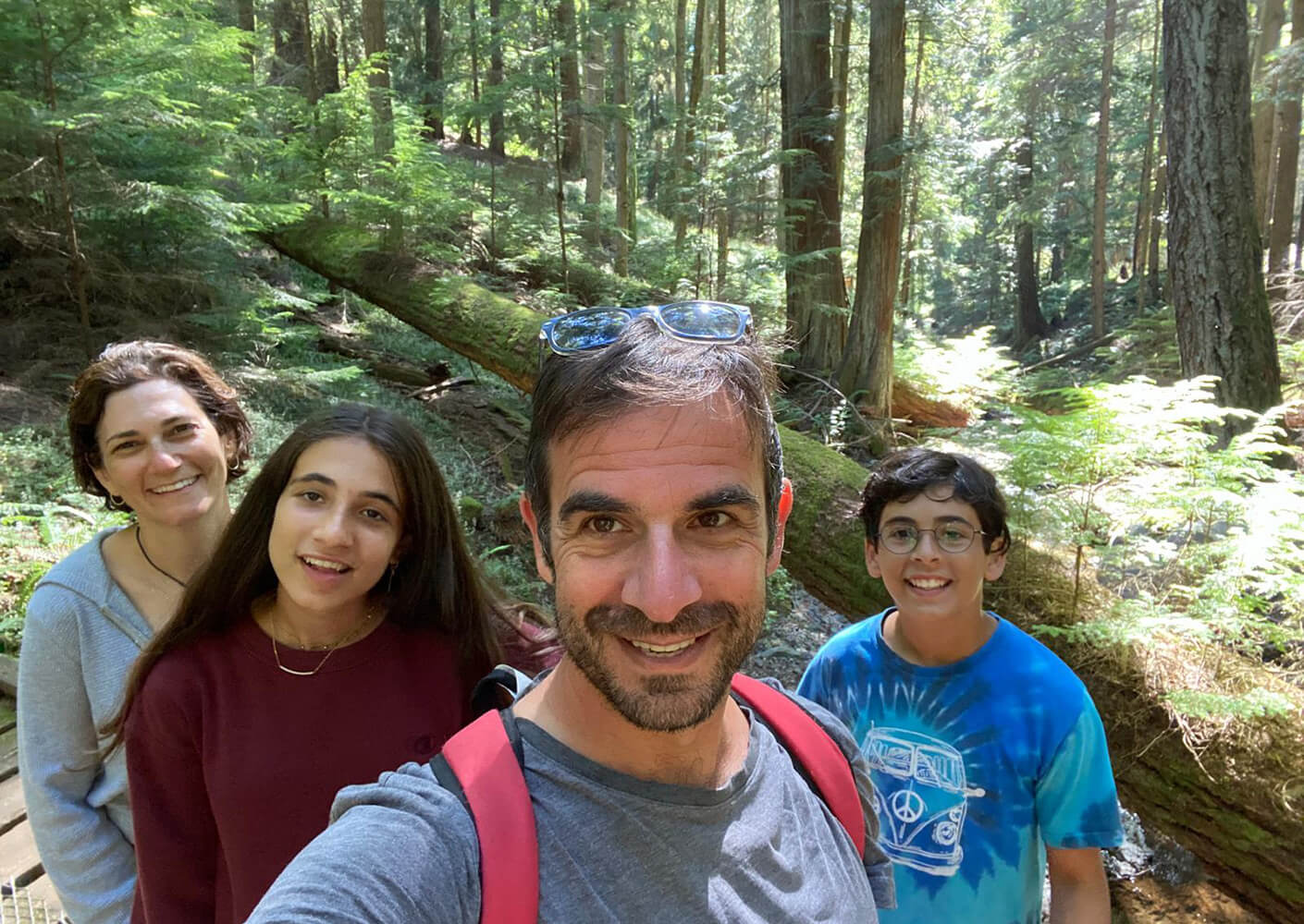 Family selfie in a forest, surrounded by trees and greenery. Four individuals smiling on a nature trail. Ideal for outdoor adventure themes.