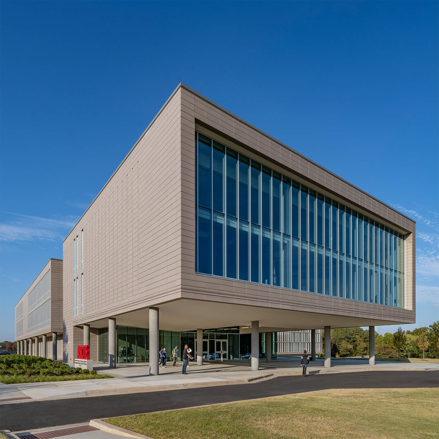 Exterior view of a building featuring large windows and a sleek design, set against a clear blue sky with people at the entrance.