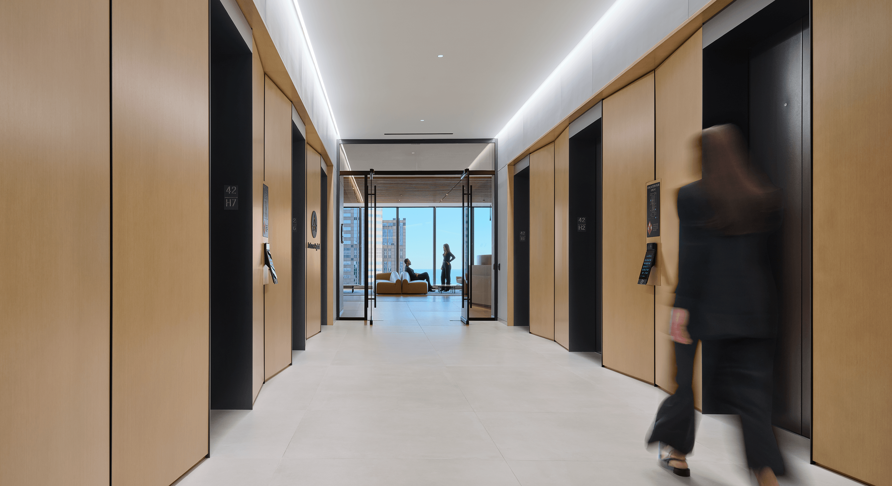 Elevator lobby with wooden paneling, several elevators labeled 42 and 2, and a view of a seating area through glass doors.