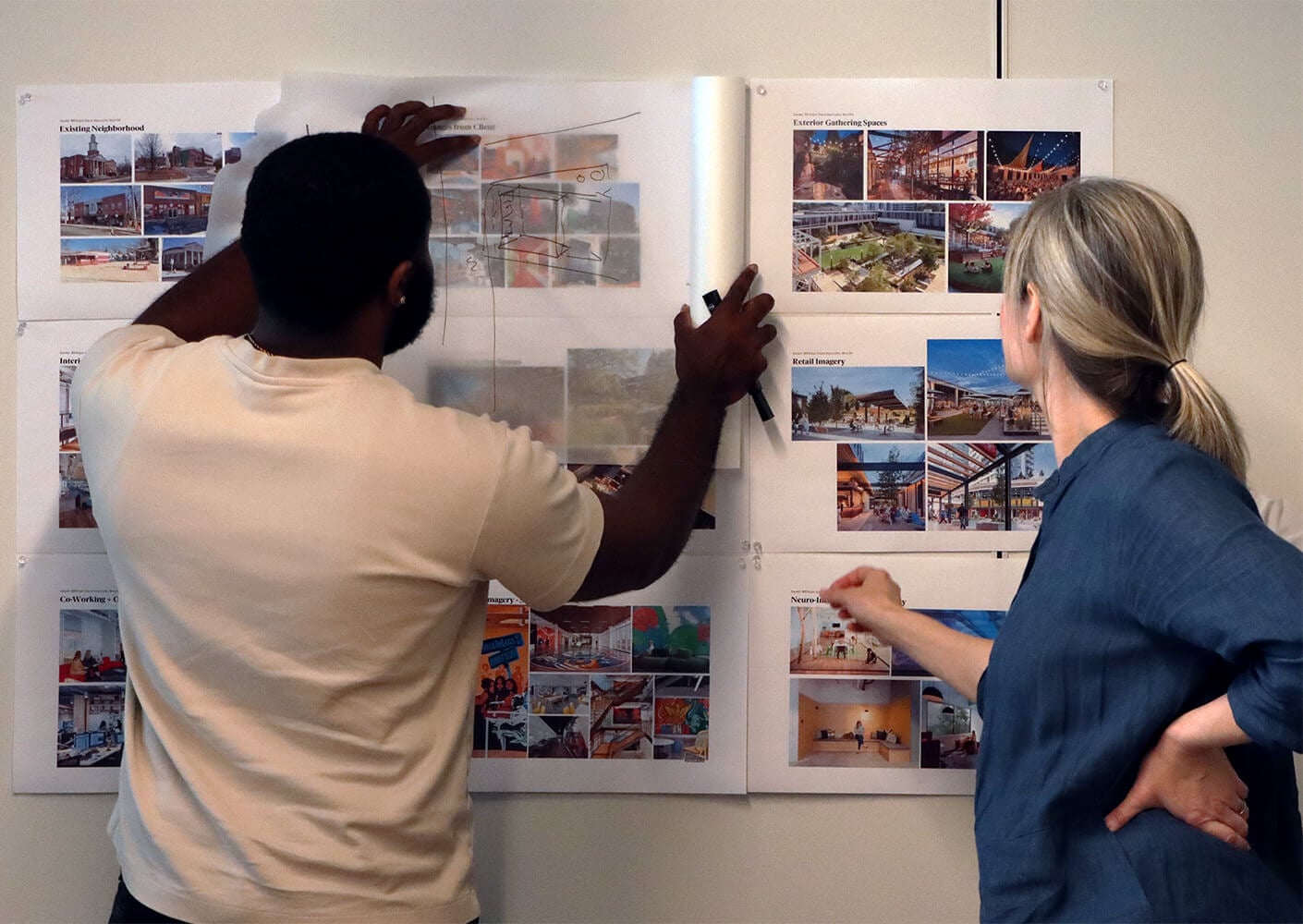 Two individuals review architectural design boards, discussing various project images and layouts for community spaces and retail designs.