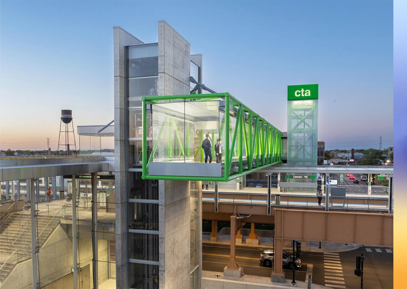 Glass bridge connecting a transit station, with two individuals inside, viewed at dusk. CTA sign and surrounding structures are visible.