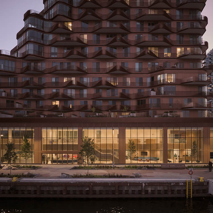 Architectural facade with wavy balcony design, large glass windows, and landscaped seating area. Evening lighting highlights interior space with community centre.