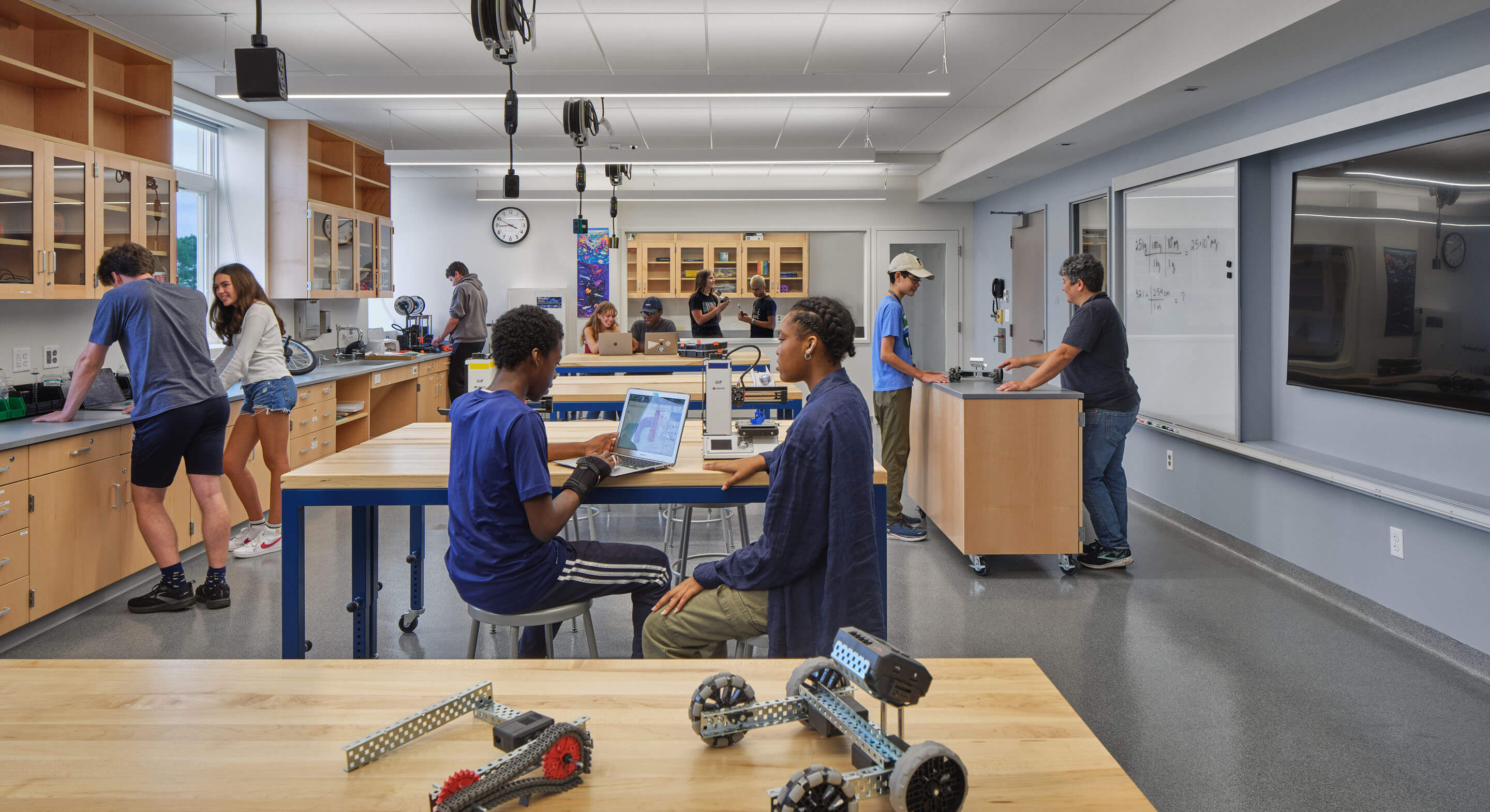Students engaged in various projects in a well-equipped classroom, featuring work tables, computers, and robotics tools.